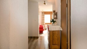 A hallway with a wooden cabinet, a red chair, and a white table with a vase of flowers.