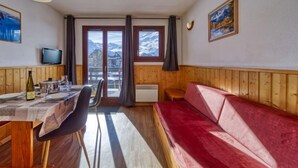 Une pièce chaleureuse avec une table en bois, des chaises, un canapé rouge, un téléviseur et une fenêtre donnant sur les montagnes.