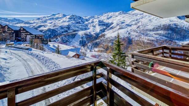 Un paysage de montagne enneigé, avec un balcon en bois donnant sur une station de ski.