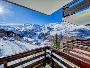 Un paysage de montagne enneigé, avec un balcon en bois donnant sur une station de ski.