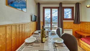 Un coin repas avec une table dressée pour quatre personnes, une bouteille de vin et un tableau représentant un paysage de montagne accroché au mur.