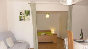 Quarto com cama, mesa de cabeceira com abajur, mesinha com garrafa e copos, e um sofá.