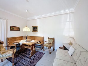 A living room with a wooden sofa, a wooden dining table with a lace tablecloth, a patterned rug, and a patterned armchair.