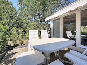 An outdoor patio with a table and chairs, surrounded by trees and a covered area with a sliding door.