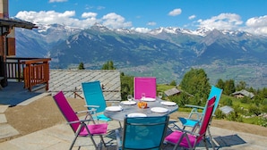 A dining table set outdoors with chairs, a view of snow-capped mountains, and a clear blue sky. - Le Ruisseau by Interhome (Nendaz)
