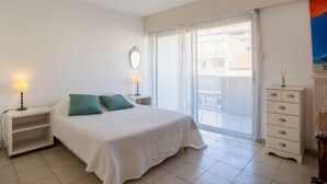 Ein Schlafzimmer mit einem Bett, einem Nachttisch, einer Kommode und einem Fenster mit Vorhängen.