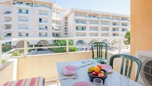 A balcony with a table set for two, a chair, and a view of a multi-story building with balconies. - Les Rives Latines by Interhome (Fréjus)