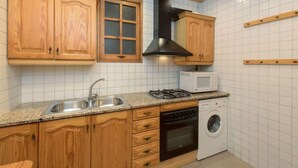 Een keuken met houten kastjes, een magnetron, een kookplaat en een wasmachine.