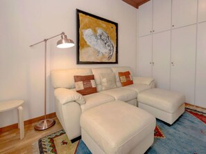 Un salon avec un canapé d’angle blanc, un lampadaire, un tapis coloré et une œuvre d’art encadrée accrochée au mur.