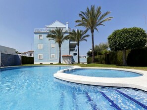 A swimming pool with a clear blue water feature, surrounded by a well-maintained lawn and palm trees.