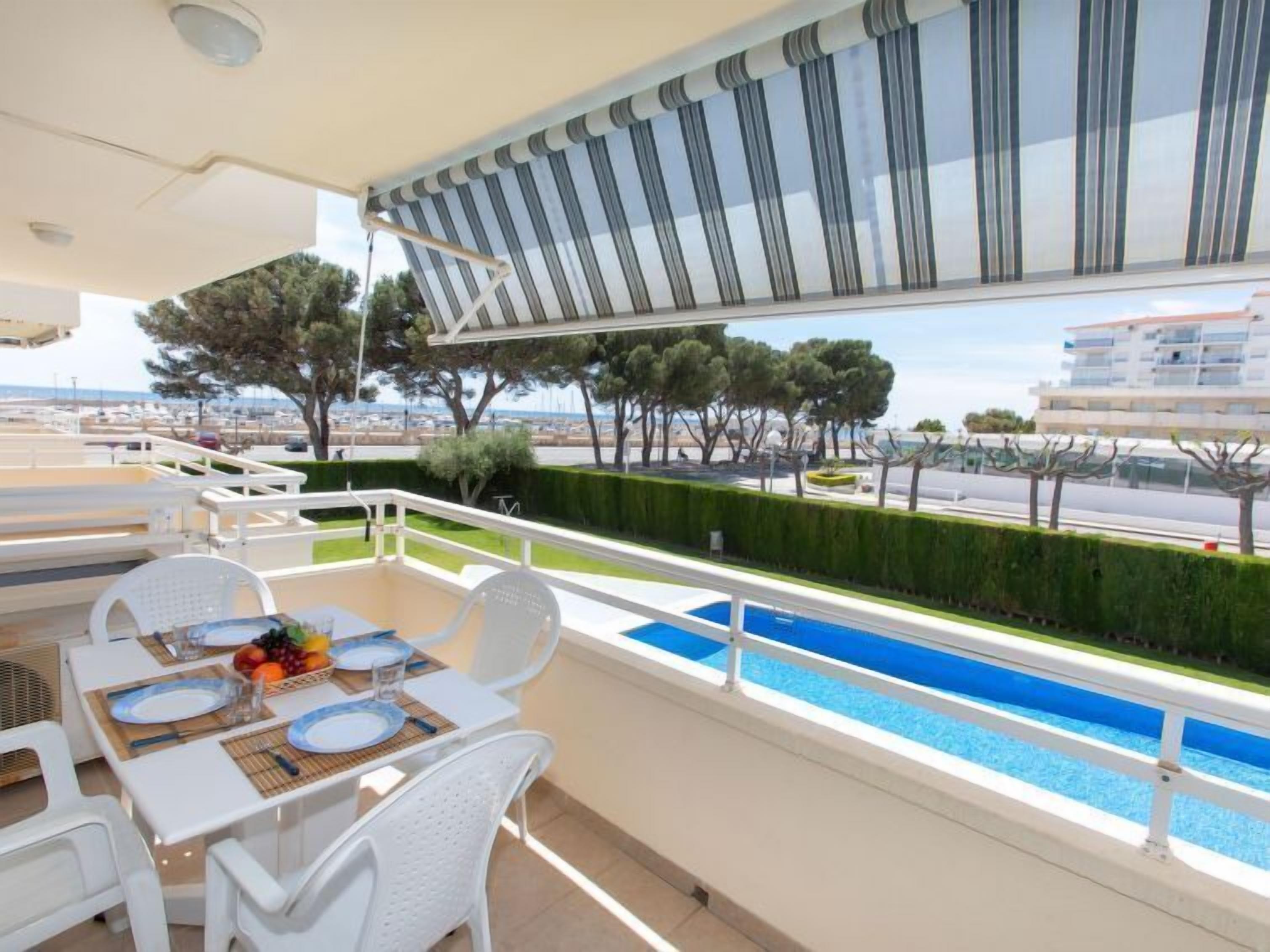 Ein Balkon mit Pool, weißen Möbeln und Blick auf das Meer und Gebäude.