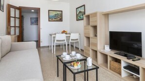 A modern living room with a sofa, a dining table with chairs, a TV, and a bookshelf. - Olivier by Interhome (Blanes)