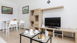 A modern living room with a TV, a glass coffee table with cups and pastries, a dining area with chairs and a table, and two paintings on the wall. - Olivier by Interhome (Blanes)