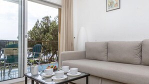 A living room with a sofa, a glass coffee table with cups and saucers, a chair, and a balcony with outdoor furniture. - Olivier by Interhome (Blanes)