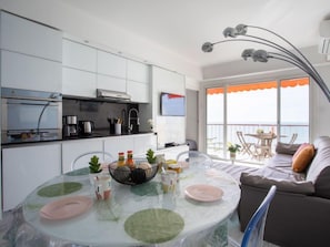 Una cucina moderna con mobili bianchi, un'area pranzo con tavolo in vetro e un balcone con vista.