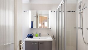 A modern bathroom with a glass shower enclosure, a white sink with a mirror above, and grey cabinets. - Casa Eduardo Apt.1 by Interhome (Ronco sopra Ascona)