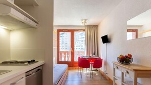 A compact hotel room with a kitchenette, a bed, a dining area with red chairs, and a small table with fruit. - Chalet Club (Val Claret) by Interhome (Tignes)