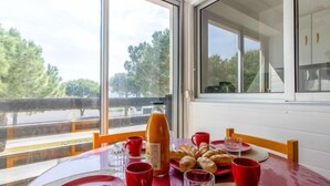 Una mesa de comedor servida con vajilla roja, una botella de zumo de naranja y pasteles, con vistas a árboles y una carretera a través de amplios ventanales.