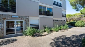 Un edificio de varios pisos con fachada de piedra, entrada de cristal y zona de estacionamiento con áreas verdes.