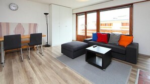 Een moderne woonkamer met een bank, voetenbankje, salontafel, en een eethoek met stoelen en een tafel.