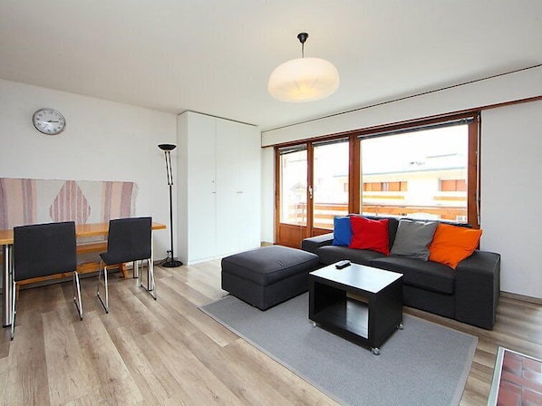 Un salon moderne comprenant un canapé, un pouf, une table basse et un coin repas avec des chaises et une table.