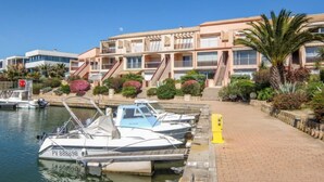 Marina com barcos atracados, edifício com várias varandas e um calçadão com paisagismo.