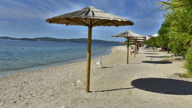 Ein Strand mit Sonnenschirmen und Liegestühlen am Ufer.