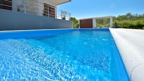 Ein moderner Poolbereich mit einem klaren, blauen Pool, einem Gebäude mit Balkon und einer Holztür im Hintergrund.