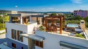 Ein modernes, zweistöckiges Gebäude mit Dachterrasse, Whirlpool und einer Holzpergola.