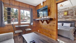 A wooden cabin room with a bed, a table, and a TV on the wall. - Juniper #105 (Big Bear Lake)