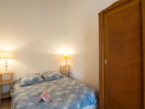 A bedroom with a bed, two bedside lamps, a wooden wardrobe, and a book on the bed.