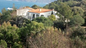 A white building with a red roof surrounded by dense green trees and mountains in the background. - Cap de Vol by Interhome (Llançà)