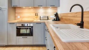 Une cuisine moderne avec des meubles gris, un plan de travail en bois, un four encastré, un grille-pain et une machine à café.