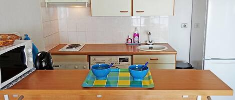 Una cocina moderna con armarios blancos, una encimera de madera, un fregadero, una estufa y un microondas. Hay dos cuencos azules sobre un mantel de cuadros en la encimera.