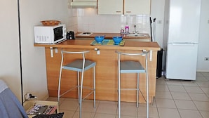 Eine kleine Küche mit einer Mikrowelle, einem Kühlschrank und einem Barhocker.