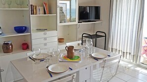 Eine moderne Küche mit weißen Schränken, einem Esstisch für vier Personen und einem an der Wand befestigten Fernseher.