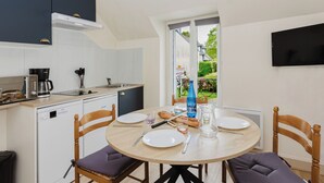 Eine kleine Küche mit Kaffeemaschine, Spüle und Geschirrspüler. Ein Esstisch mit Stühlen und ein Fenster mit Blick nach draußen.