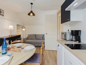 A compact kitchen with a dining area, a sofa, and a coffee maker.