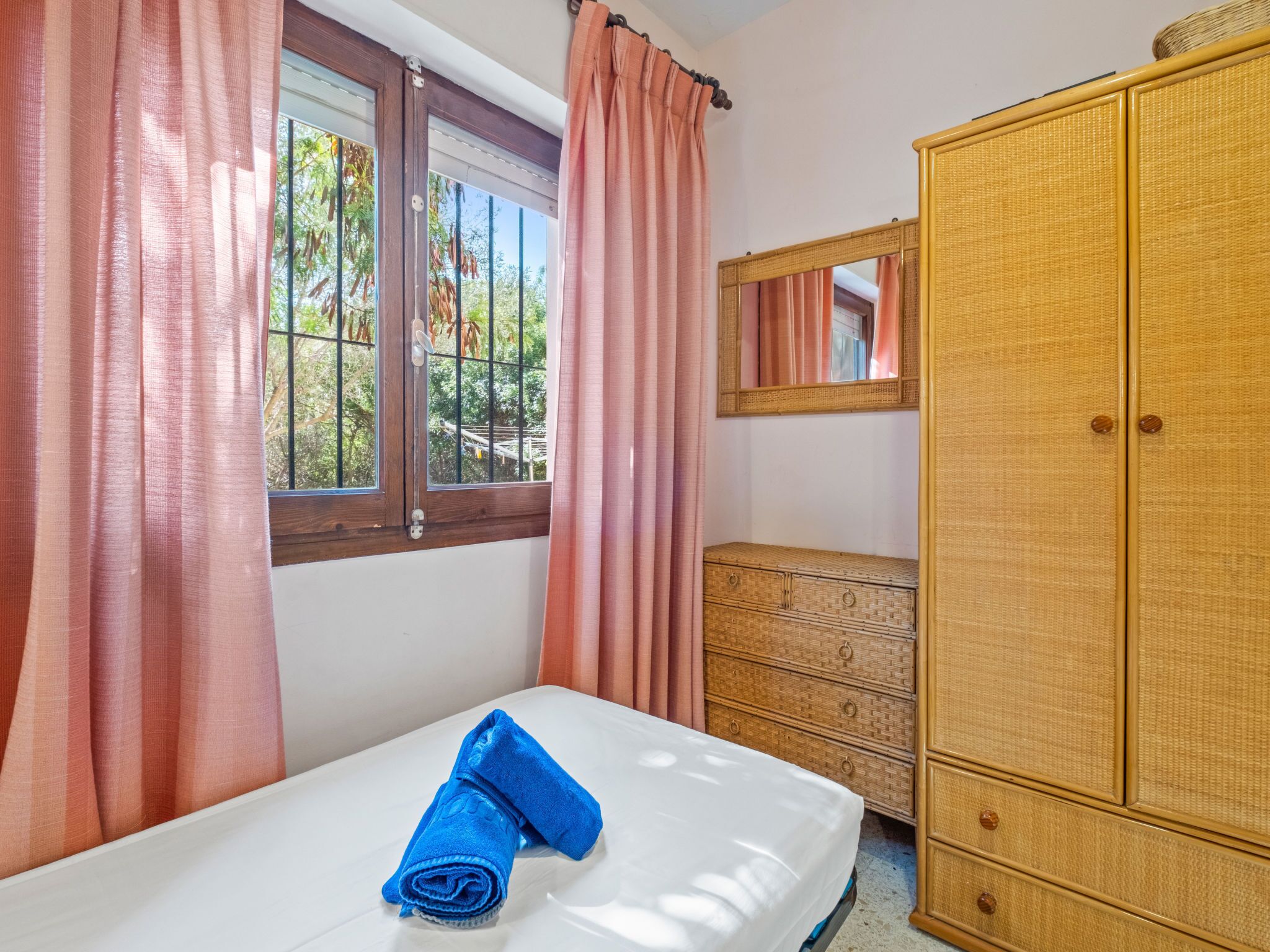 Ein Zimmer mit einem Bett, einem Holzschrank, einem Spiegel und einem Fenster mit Vorhängen.