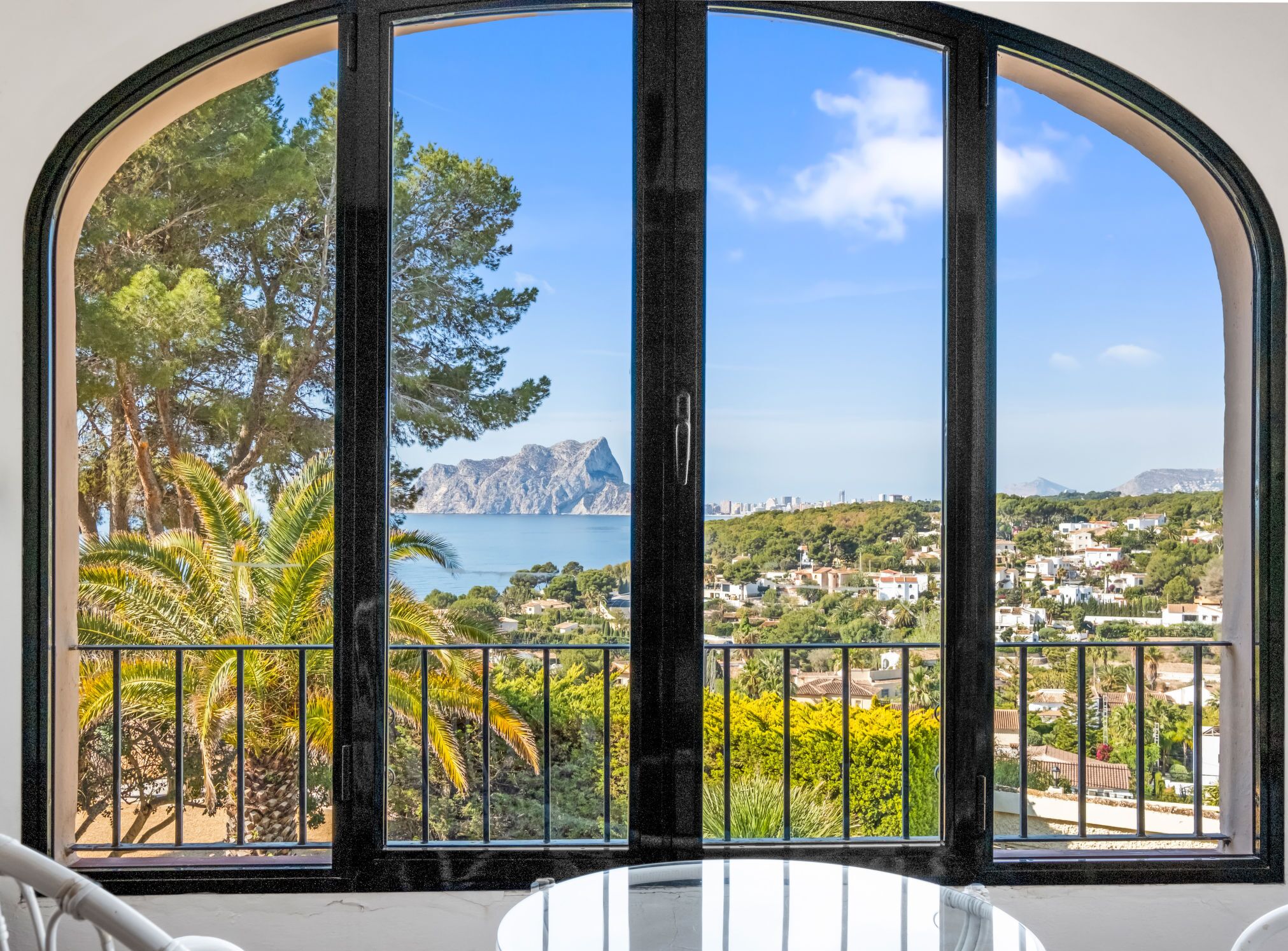 Ein Zimmer mit einem großen Bogenfenster, das Blick auf eine Küstenlandschaft bietet, darunter Bäume, ein Berg und ein Gewässer.