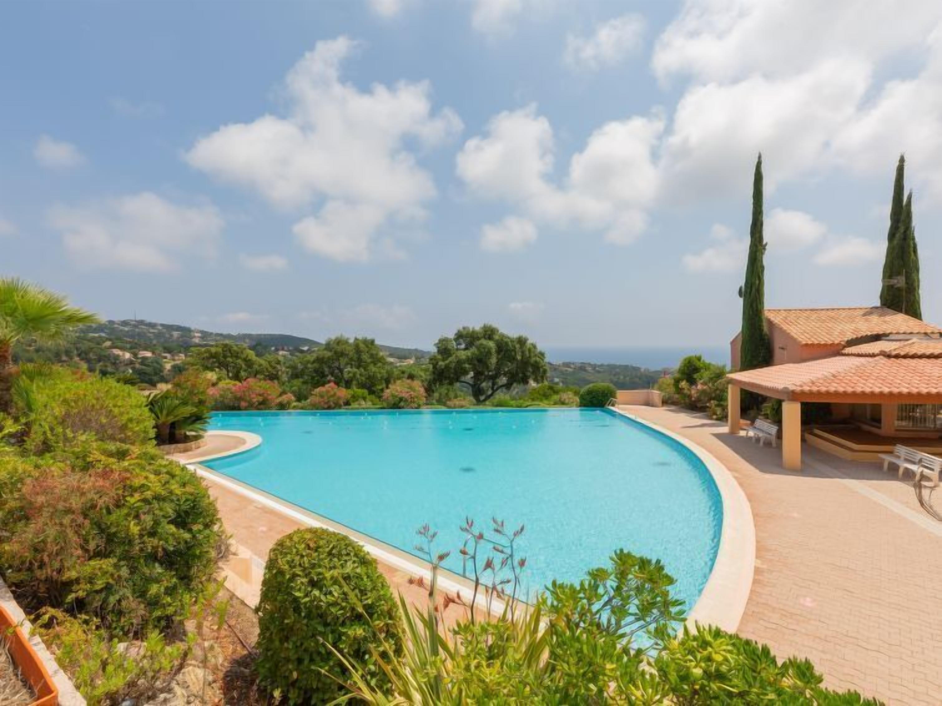 A swimming pool with a curved edge, surrounded by lush greenery and a view of the sea.
