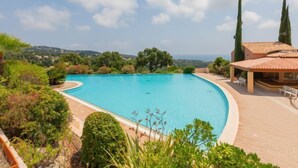 A swimming pool with a curved edge, surrounded by lush greenery and a view of the sea.
