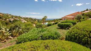 A hillside property with a large house, lush greenery, and a view of the sea.