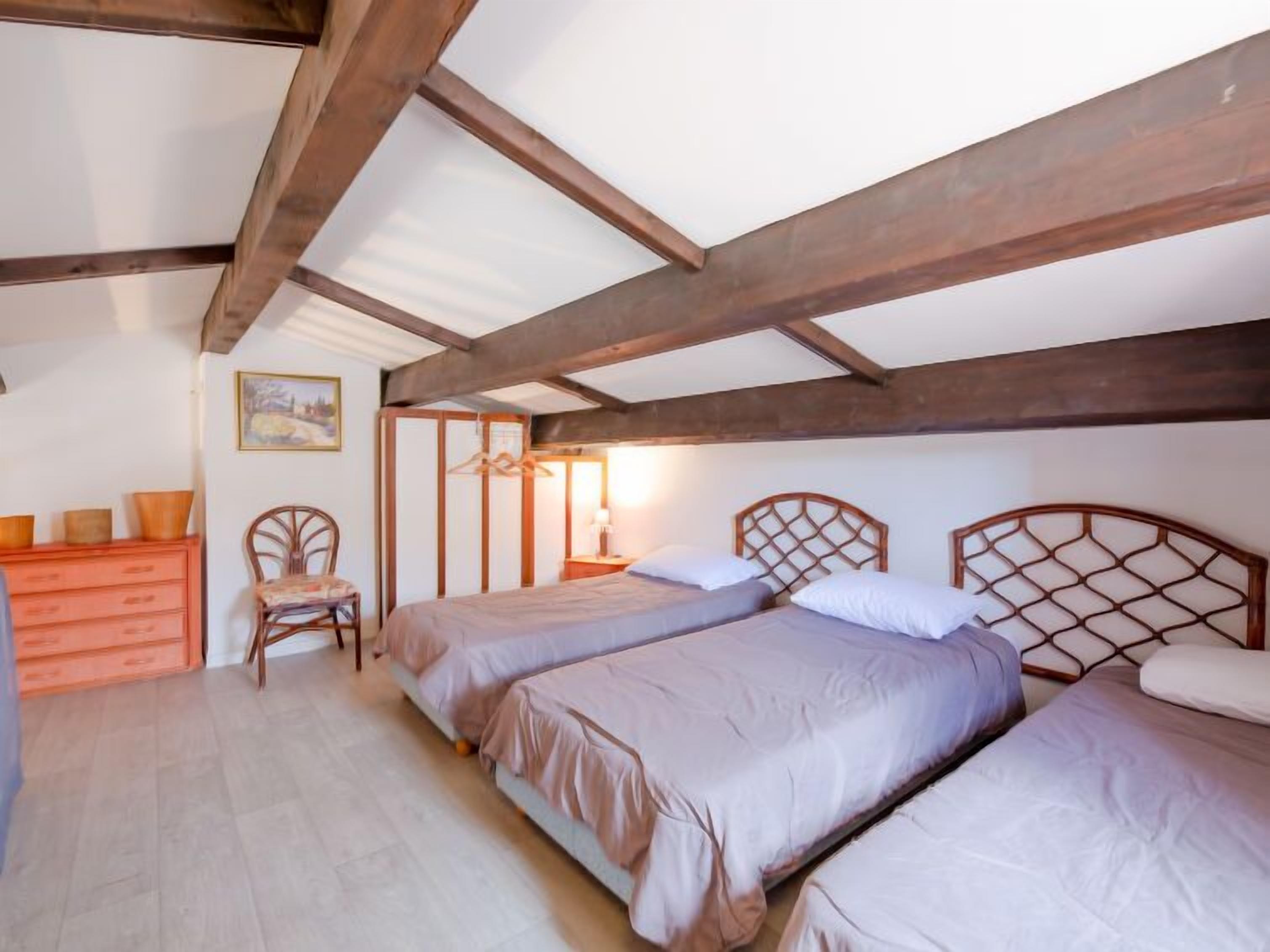 A bedroom with two beds, wooden beams, a dresser, and a chair.