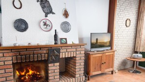 Un salon chaleureux avec une cheminée en briques, un téléviseur et un petit meuble en bois.
