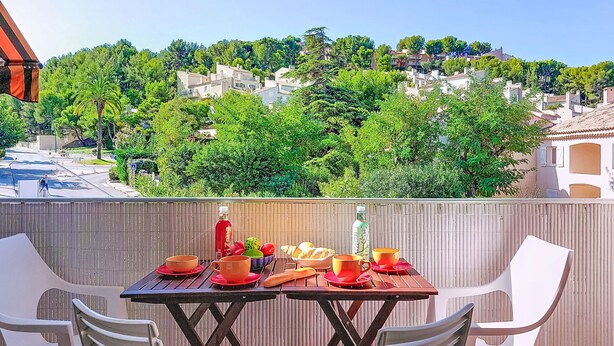 Ein Balkon mit Tisch für zwei Personen, Blick auf eine Wohngegend mit Bäumen und Häusern.