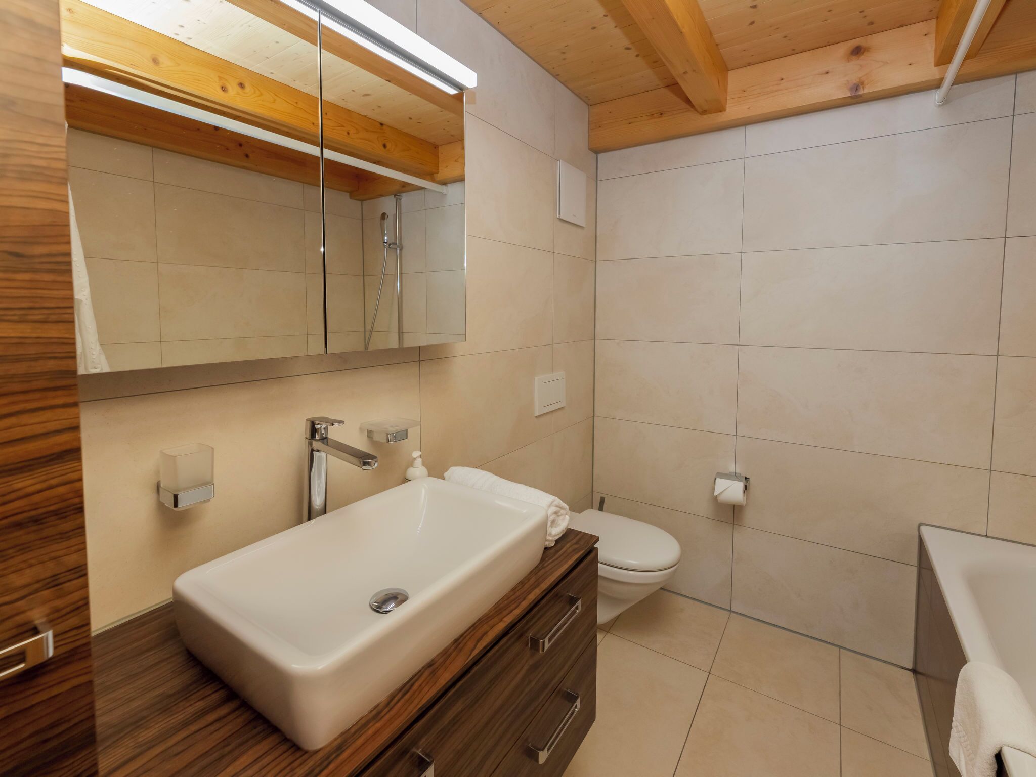 A modern bathroom with a wooden vanity, a large mirror, a toilet, and a shower area.