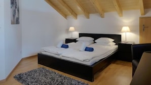 A bedroom with a wooden ceiling, a black bed frame, white bedding, two bedside lamps, and a gray rug. - Staubbach by Interhome (Lauterbrunnen)