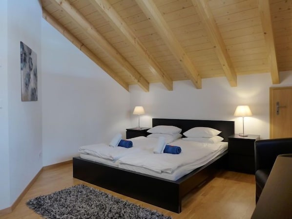 A bedroom with a wooden ceiling, a black bed frame, white bedding, two bedside lamps, and a gray rug.
