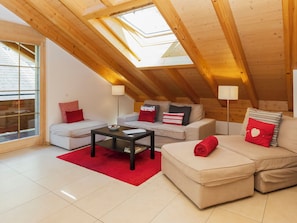 A modern loft bedroom with a sloped ceiling, skylight, and a cozy seating area with a sofa and a coffee table.